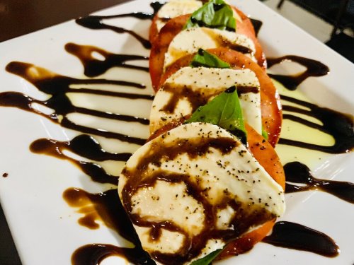 A plate of Caprese salad with sliced tomatoes, mozzarella, basil, and drizzled balsamic glaze.