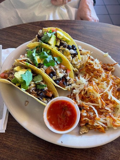 Three tacos filled with meat, beans, and toppings, served with hash browns and a side of salsa.