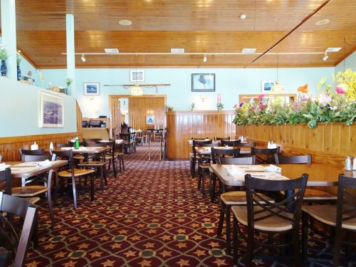 Interior of a restaurant featuring wooden decor, tables set for dining, and floral arrangements along the walls.