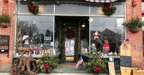 A festive storefront decorated with wreaths, Christmas items, and flags, inviting customers inside.