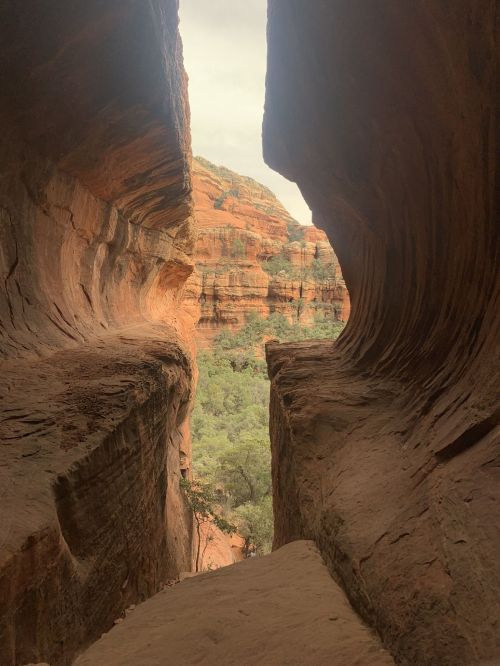 A narrow rock formation frames a view of lush greenery and layered cliffs in a canyon landscape.