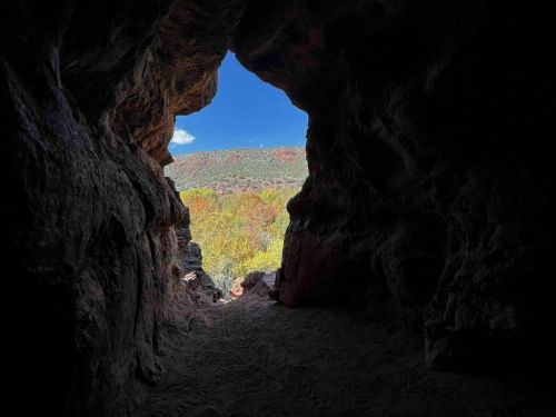View from inside a cave, looking out at a colorful landscape and blue sky.