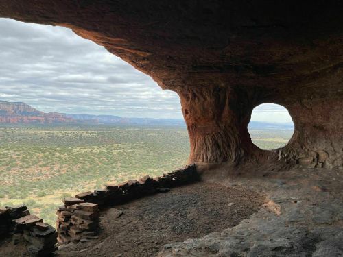 View from inside a cave, featuring a large circular opening and a scenic landscape of hills and valleys beyond.