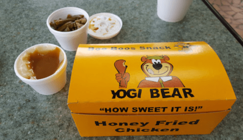 A yellow takeout box labeled "Yogi Bear" with honey fried chicken, sides of green beans, and mashed potatoes.