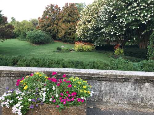 A lush garden with colorful flowers in a planter, surrounded by green trees and blooming shrubs.