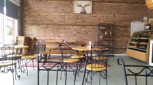 Cozy café interior with wooden tables, metal chairs, and a brick wall, featuring a display case and a deer painting.