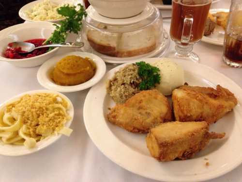 A plate of fried chicken with sides of mashed potatoes, stuffing, pumpkin, and pasta, accompanied by drinks and salad.