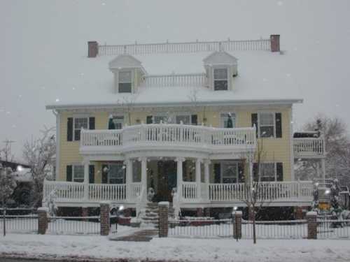 A large yellow house with white trim, featuring multiple balconies, surrounded by snow on a winter day.