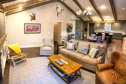 Cozy living room with a mix of modern and rustic decor, featuring a sofa, armchair, coffee table, and wooden beams.