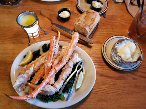 A plate of crab legs with lemon, served with bread, butter, and a side of mashed potatoes on a wooden table.