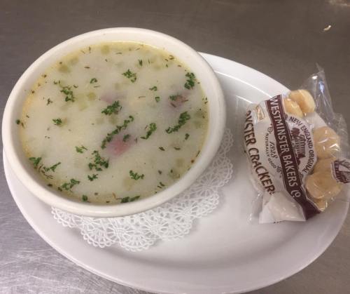 A bowl of creamy soup garnished with herbs, served with a side of crackers on a white plate.