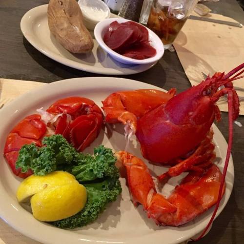 A plate featuring a whole lobster, lobster claws, lemon, kale, and a side of sweet potato and pickled beets.