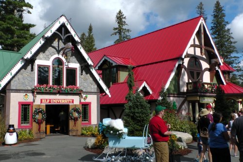 A festive building with a red roof and holiday decorations, featuring "Elf University" signage and people gathered outside.