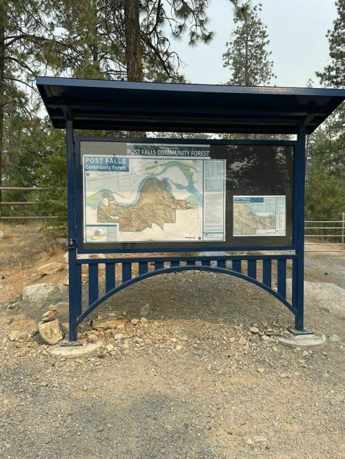Information sign for Post Falls Community Forest, featuring a map and details about the area, surrounded by trees.