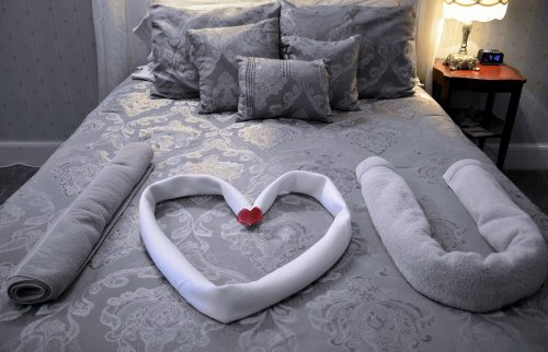 A neatly made bed with decorative pillows and towels arranged to spell "I LOVE U" with a small red heart.