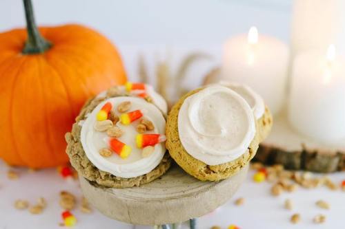 Two decorated cookies on a wooden stand, surrounded by candy corn, pumpkin, and candles, creating a festive autumn scene.