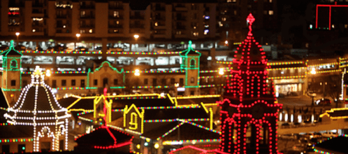 Colorful holiday lights illuminate buildings and structures at night, creating a festive atmosphere.