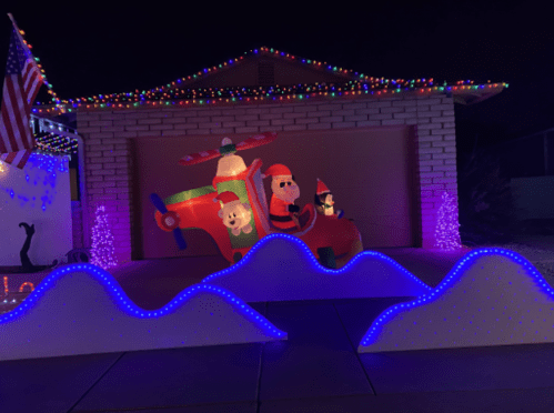 A festive display featuring inflatable Santa in a plane, with colorful lights and wave-shaped decorations in front.