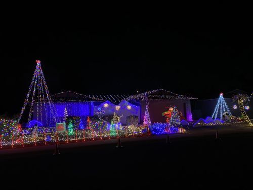 A festive house decorated with colorful Christmas lights, featuring trees and various holiday displays at night.
