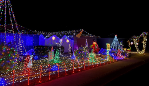 A festive display of colorful Christmas lights adorning a house and yard, featuring trees, snowmen, and decorations.