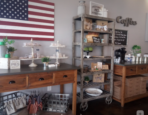 A cozy café interior featuring a wooden table, display shelves with baked goods, and American flag decor.