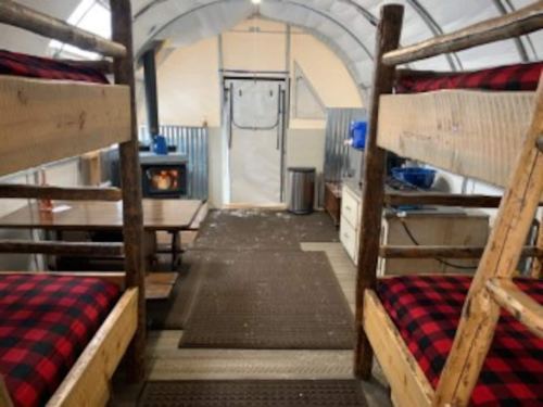 Interior of a cozy cabin with bunk beds, a table, and a wood stove, featuring rustic decor and a warm atmosphere.