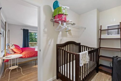 A cozy room featuring a crib, a colorful bed, and a shelf with baby supplies, with natural light coming through the window.