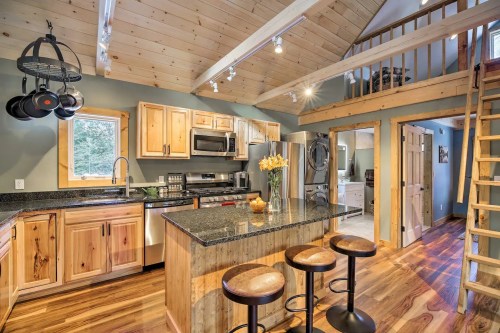 Cozy kitchen with wooden cabinets, granite island, and bar stools, featuring an open layout and a lofted area above.