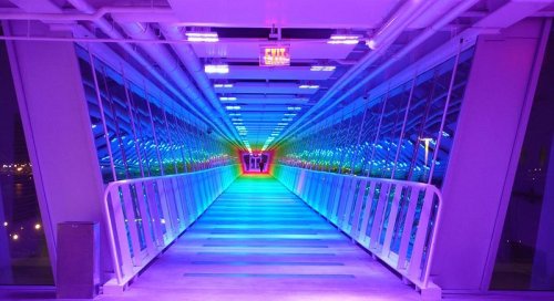 A brightly lit, colorful corridor with mirrored walls creating a vibrant, tunnel-like effect.