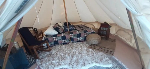 Cozy tent interior with a bed, rocking chair, decorative pillows, and soft rugs, creating a warm, inviting atmosphere.