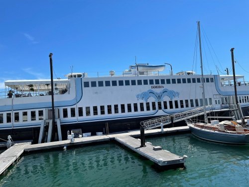 A large ferry docked at a marina, with a clear blue sky and a small sailboat nearby.
