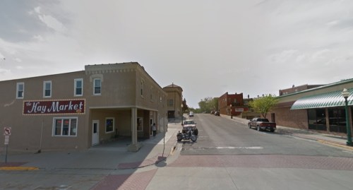 A street view of a small town featuring shops, parked cars, and a clear sky.