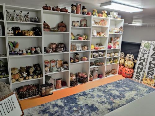 A cozy display of seasonal decorations, including pumpkins, plush toys, and festive signs on white shelves.
