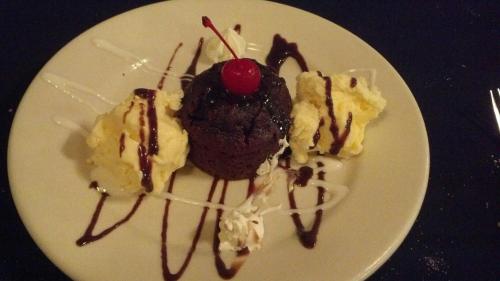 A chocolate dessert with a cherry on top, surrounded by scoops of vanilla ice cream and drizzled with chocolate sauce.