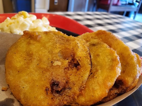 Three golden, crispy fried plantains served with a side of macaroni and cheese on a checkered tablecloth.
