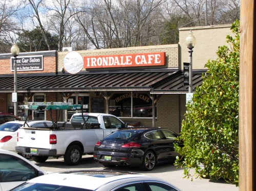Exterior view of Irondale Cafe, featuring a sign and parked cars, surrounded by trees and buildings.