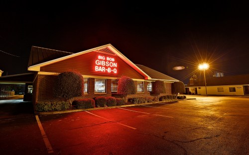 A barbecue restaurant at night, featuring a bright red sign that reads "Big Bob Gibson Bar-B-Q" and illuminated parking lot.