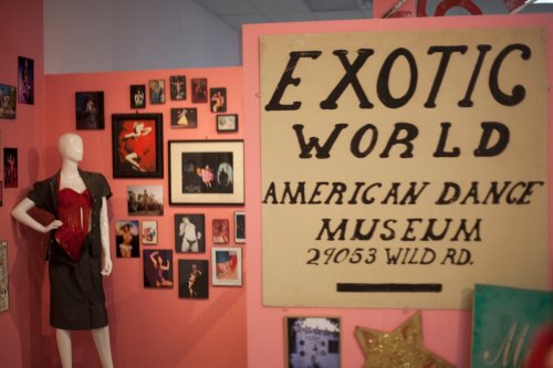 A display featuring a mannequin in a dress, framed photos, and a sign for the Exotic World American Dance Museum.