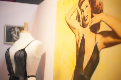 A mannequin displays a black dress next to a vintage portrait of a woman in a similar style.