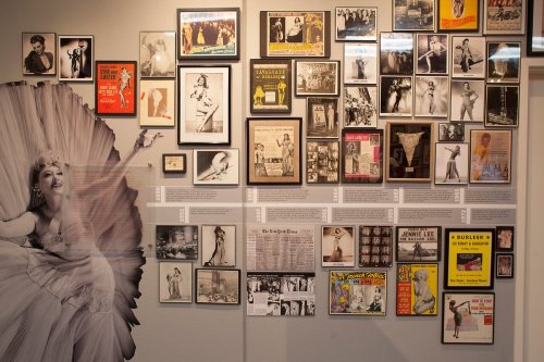 A gallery wall featuring various framed photographs and posters, including a large image of a performer in a dramatic pose.