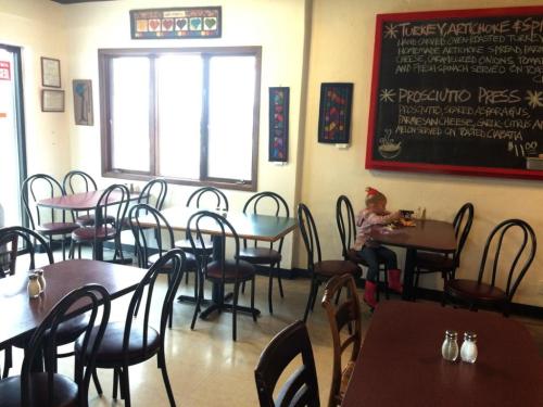A cozy café interior with empty tables and a child sitting at a table, enjoying a meal by the window.