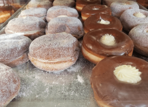 A variety of donuts, including powdered and chocolate-frosted, displayed on a tray.