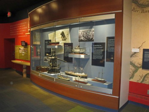 Display case featuring various ship models and historical maritime artifacts in a museum setting.