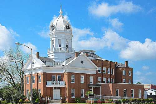 Historic brick building with a white clock tower, surrounded by blue skies and fluffy clouds.