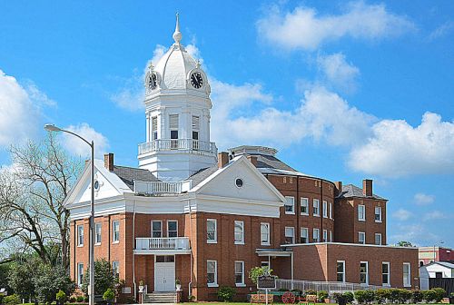 Historic brick building with a white clock tower, surrounded by blue skies and fluffy clouds.