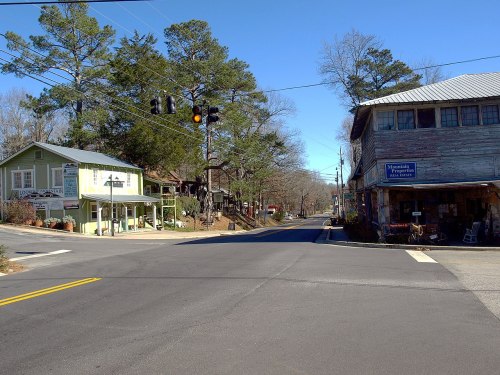 A quiet intersection in a small town, featuring quaint buildings and trees under a clear blue sky.