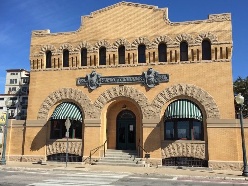 Historic yellow brick building with decorative arches and green-striped awnings, set against a clear blue sky.