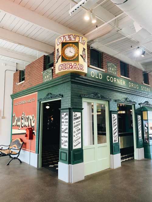 A vintage-style drug store with a green facade, clock tower, and signs, resembling an old corner shop.