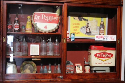 Display case featuring vintage Dr Pepper memorabilia, including bottles, signs, and an ice cream cooler.