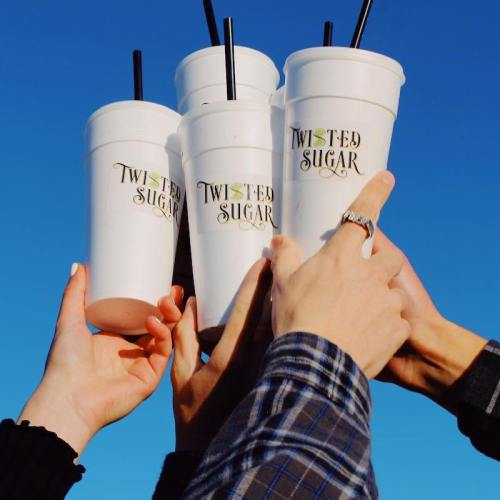 Four hands holding large cups with "Twisted Sugar" logos against a clear blue sky.
